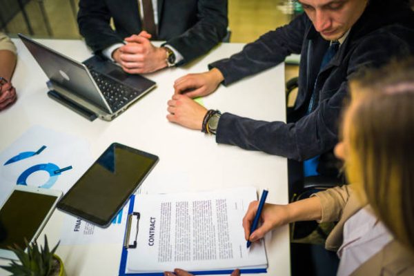 Business woman signing paper contract at group meeting