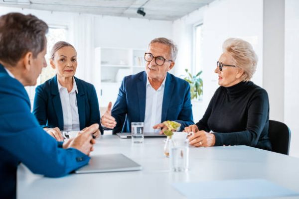 Senior businesswomen and businessmen wearing elegant suits sitting at the table in the office and discussing during business meeting.