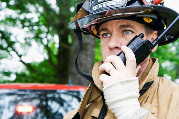 A fireman looks off camera as he talks on his radio.