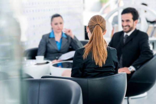 Business woman and businessmen sitting by the table and interviewing young woman sitting on the other side of the table,  blurred background